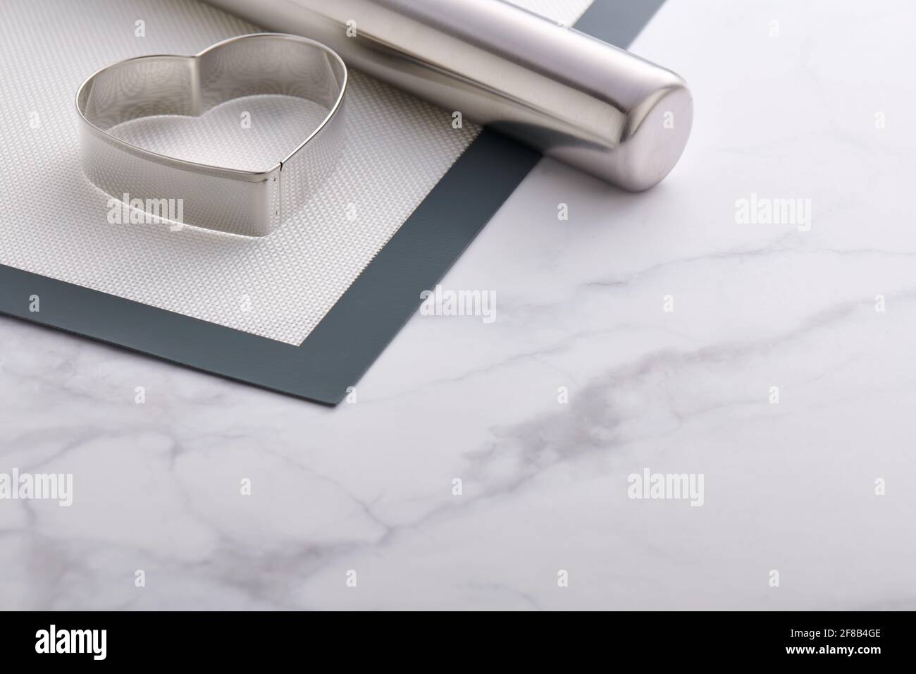 Taglierina per biscotti a forma di cuore in acciaio inox e perno di rotolamento su cui poggiare una stuoia da forno Foto Stock