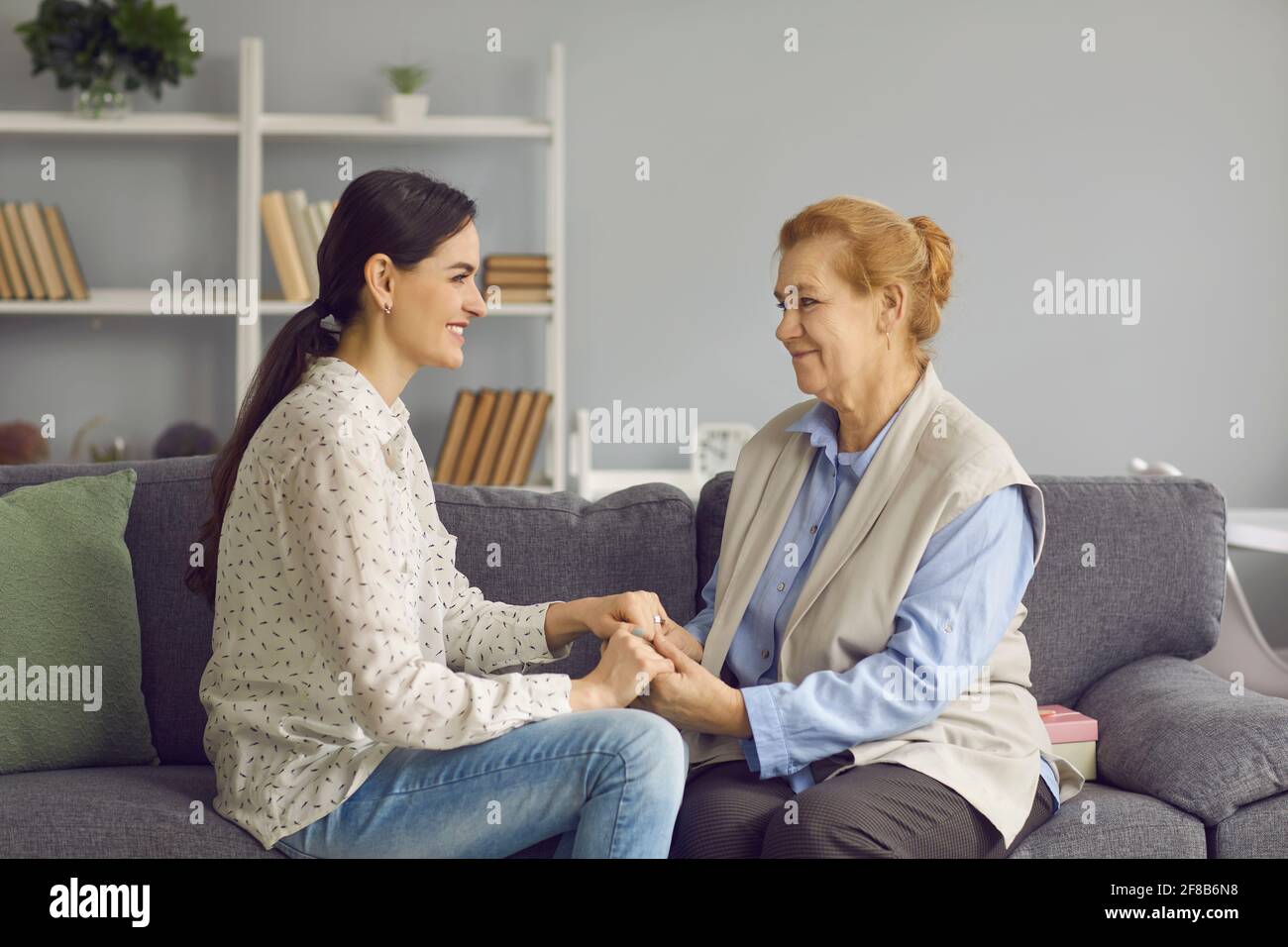 Sorridente madre anziana e figlia adulta che tengono insieme le mani siedono sul divano Foto Stock