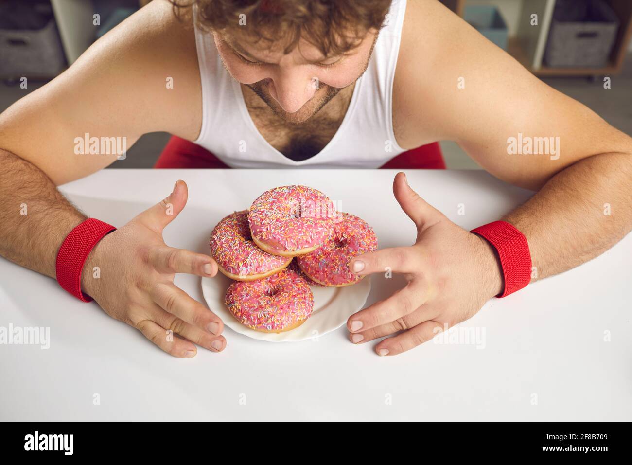 Da sopra colpo di un uomo chubby felice che guarda un piatto di allettanti ciambelle zuccherate Foto Stock