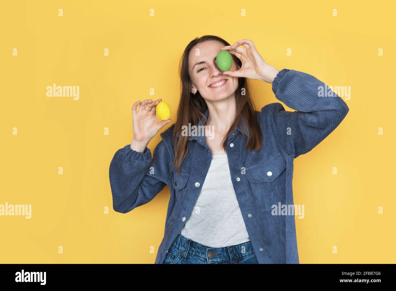 La ragazza chiude gli occhi con le uova, isolate su sfondo giallo Foto Stock