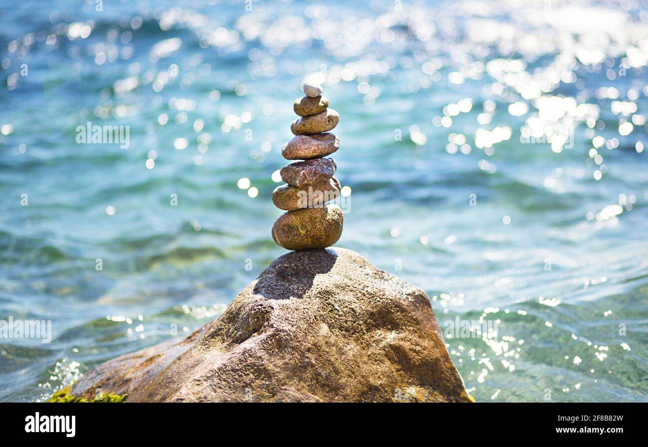 Una piramide di ciottoli su una grande pietra sullo sfondo del mare e il sole che si affaccia sull'acqua. Tour, turismo, vacanza in resort, swimm Foto Stock