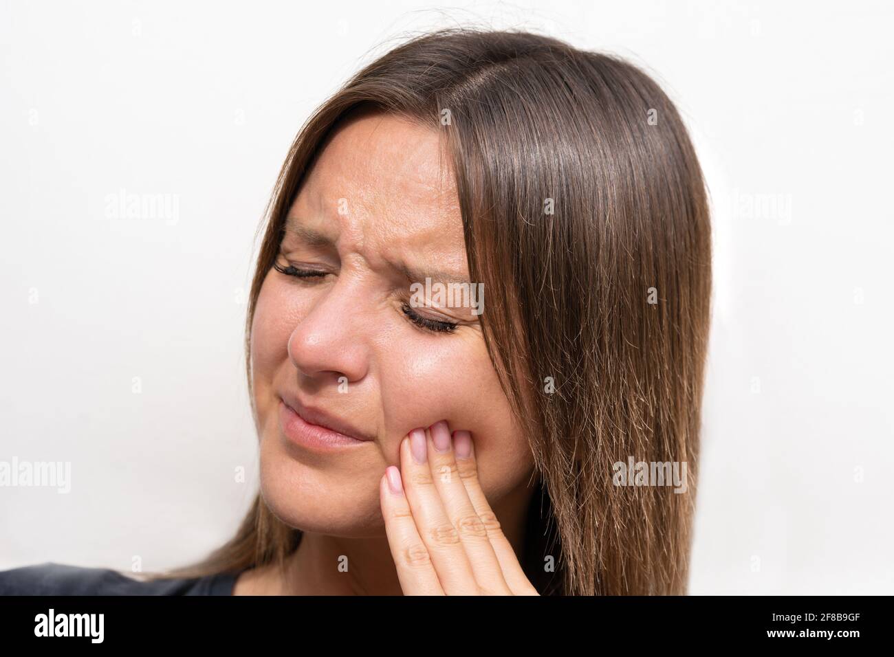 Giovane donna che tocca la guancia a causa del forte dolore ai denti. Donna che soffre di mal di denti. Faccia della donna con espressione dolorosa. Problema ai denti Foto Stock