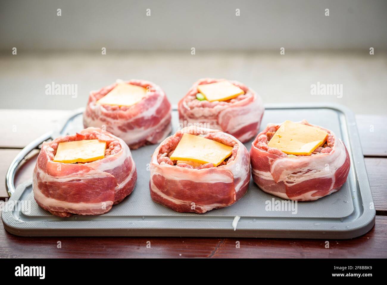 Rendendo fatta in casa birra può Bacon gli hamburger sul grill barbecue. La preparazione di polpette ripiene, avvolto in pancetta. Foto Stock