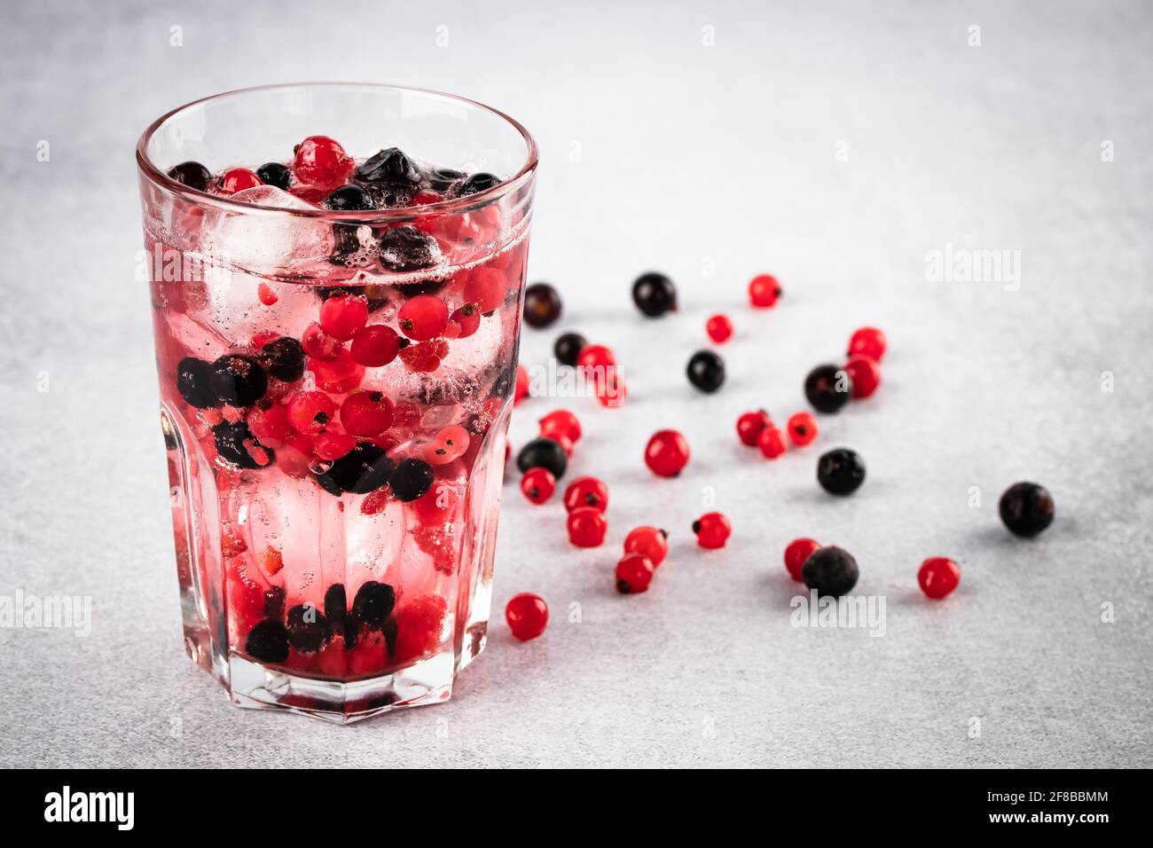 Bicchiere di ribes rosso. Bevanda estiva rinfrescante con ribes nero e ghiaccio da vicino su sfondo grigio. Fruitarismo, concetto di veganismo. Vegetariano Foto Stock