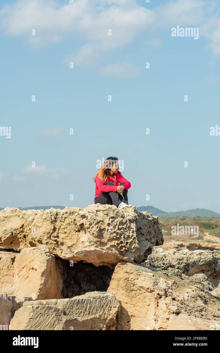 Ragazza latina, seduta su una roccia di pietra, indossando occhiali da sole, prendere il sole e pensare Foto Stock