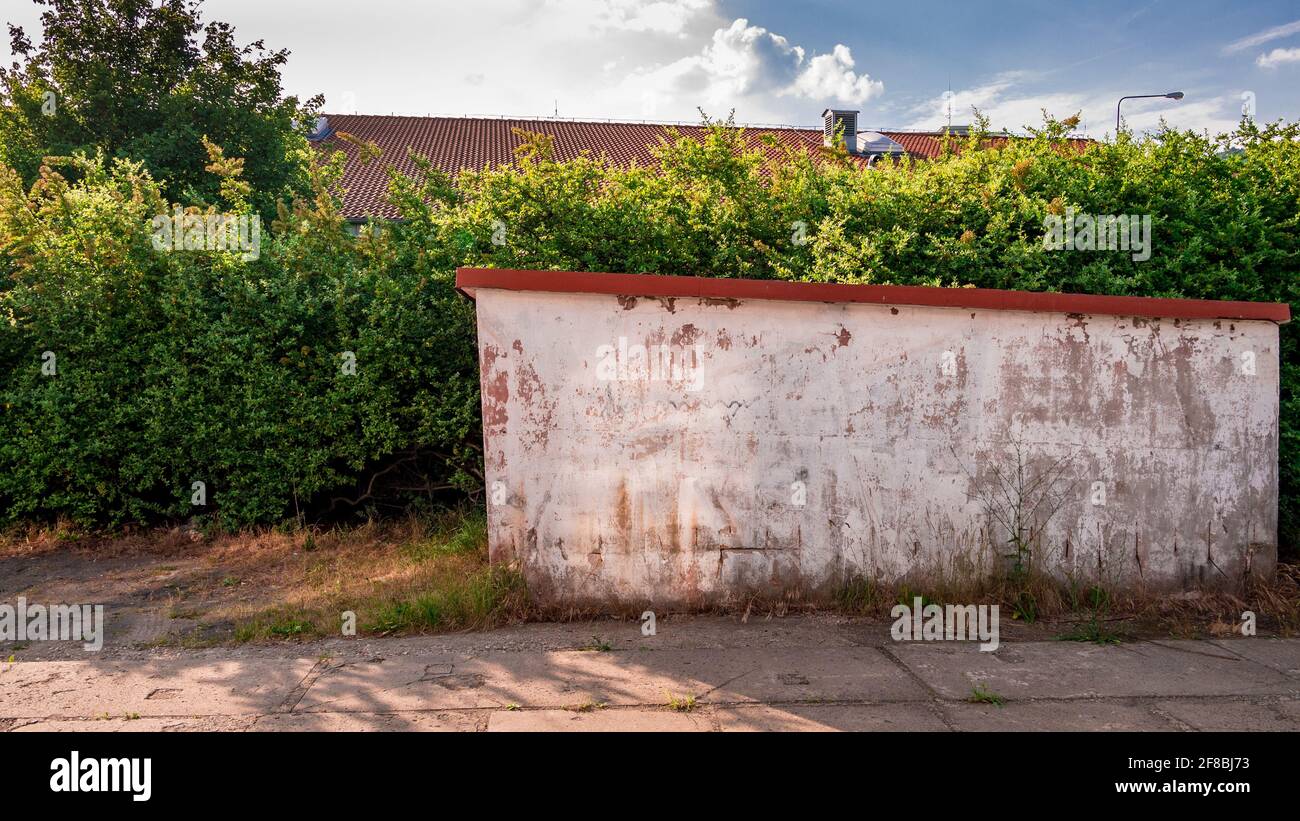 La parete incrinata del garage di fronte al cespugli che formano la siepe Foto Stock
