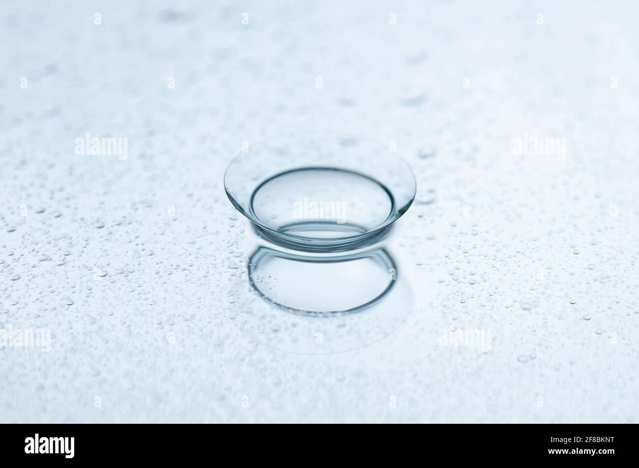 Lente a contatto con gocce d'acqua su uno sfondo a specchio. Foto Stock