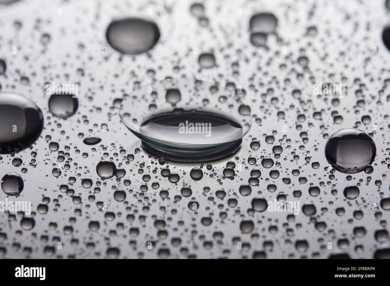 Lente a contatto con gocce su sfondo lucido. Foto Stock