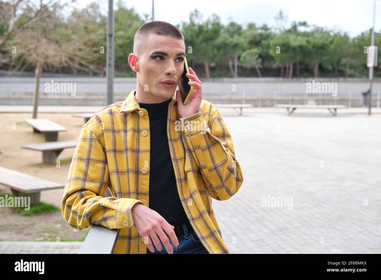 Giovane non binaria che parla dal suo smartphone. Make up persona androgina. Foto Stock