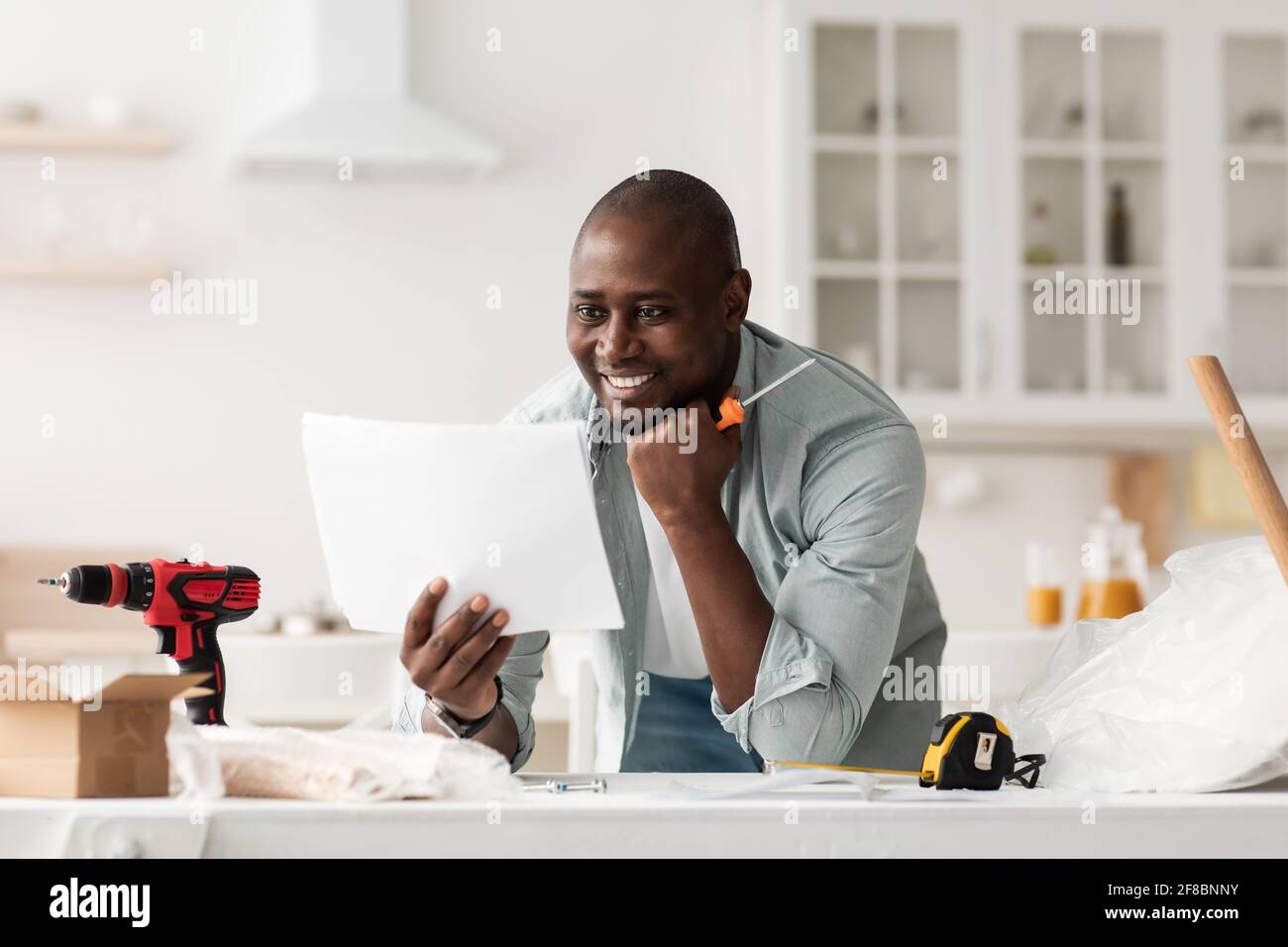 Buon uomo nero che legge le istruzioni di installazione, tenendo il cacciavite nell'interno della cucina Foto Stock