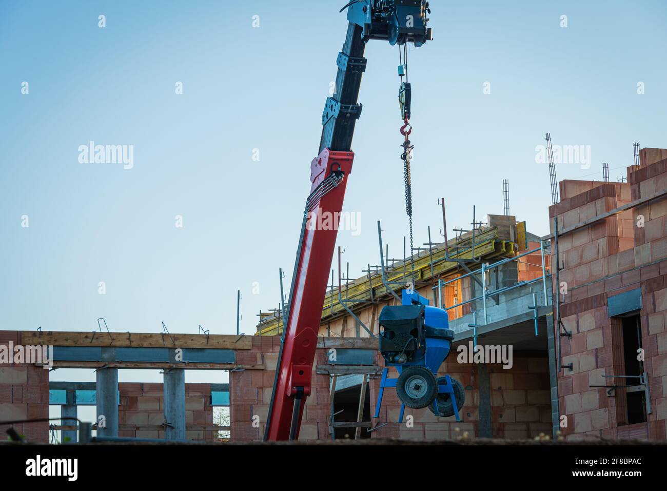 Betoniera o cassoniera blu appesa al carrello elevatore telescopico rosso in un cantiere francese, antifurto Foto Stock