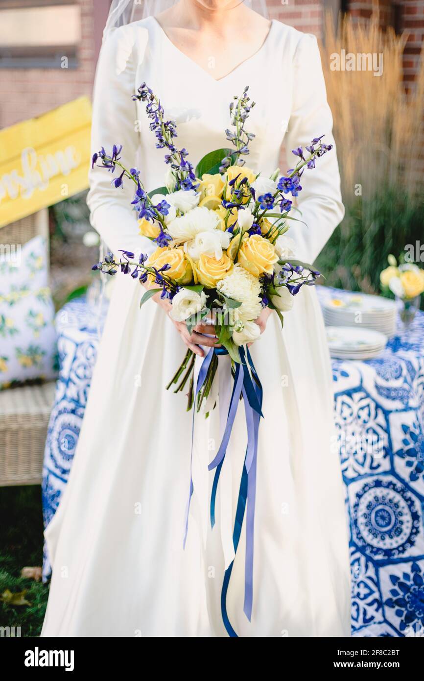 La sposa tiene il bel bouquet vibrante di nozze di giallo e bianco rose con accenti blu scuro Foto Stock