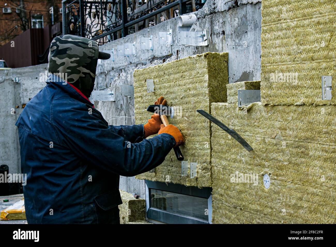 Un uomo installa uno strato di isolamento termico sulla parete delle scale all'esterno - utilizzando pannelli di lana minerale. Il concetto di riparazione e isolamento di es Foto Stock
