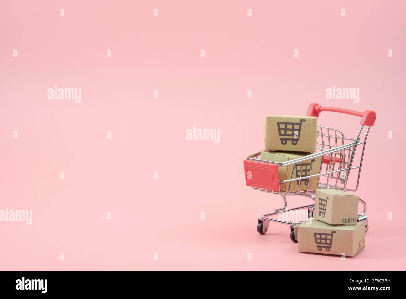 Concetto di shopping - cartoni o scatole di carta nel carrello di shopping rosso su sfondo rosa. I consumatori di shopping in linea possono acquistare da casa e servizio di consegna. Foto Stock