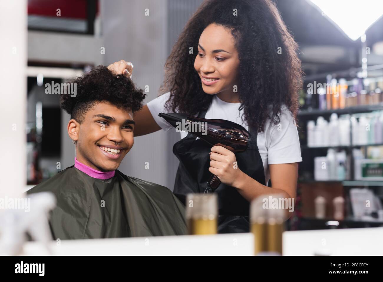 Cliente sorridente che guarda lo specchio vicino al parrucchiere con  asciugacapelli in salone Foto stock - Alamy