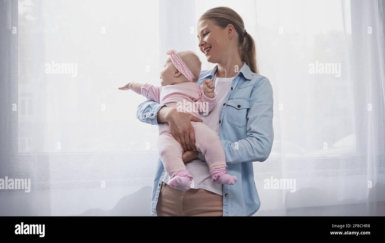 gioiosa madre che tiene in braccio la figlia del bambino che punta con la mano alla finestra Foto Stock