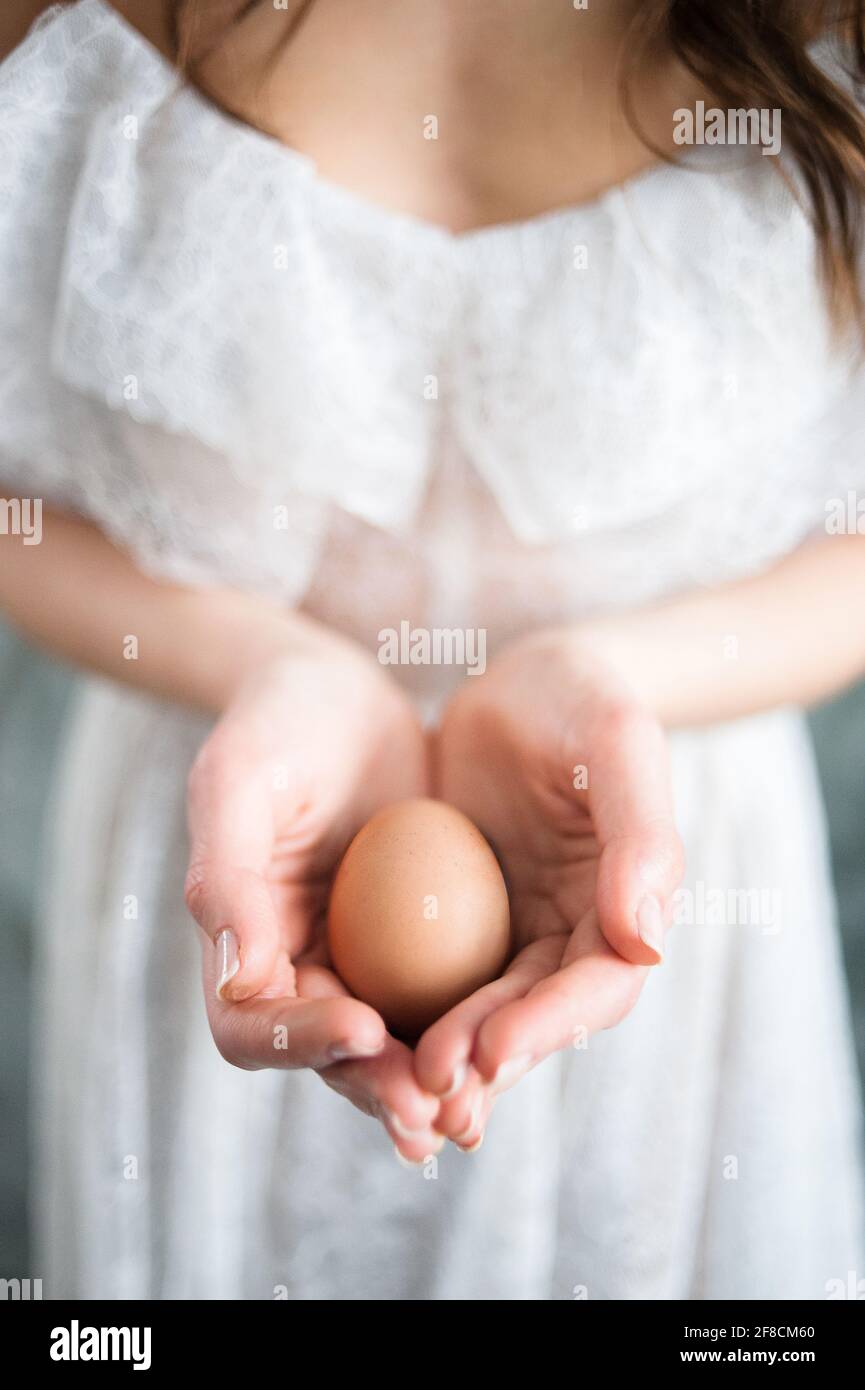 Uovo di Pasqua nelle palme di una donna in un primo piano vestito bianco. Foto Stock