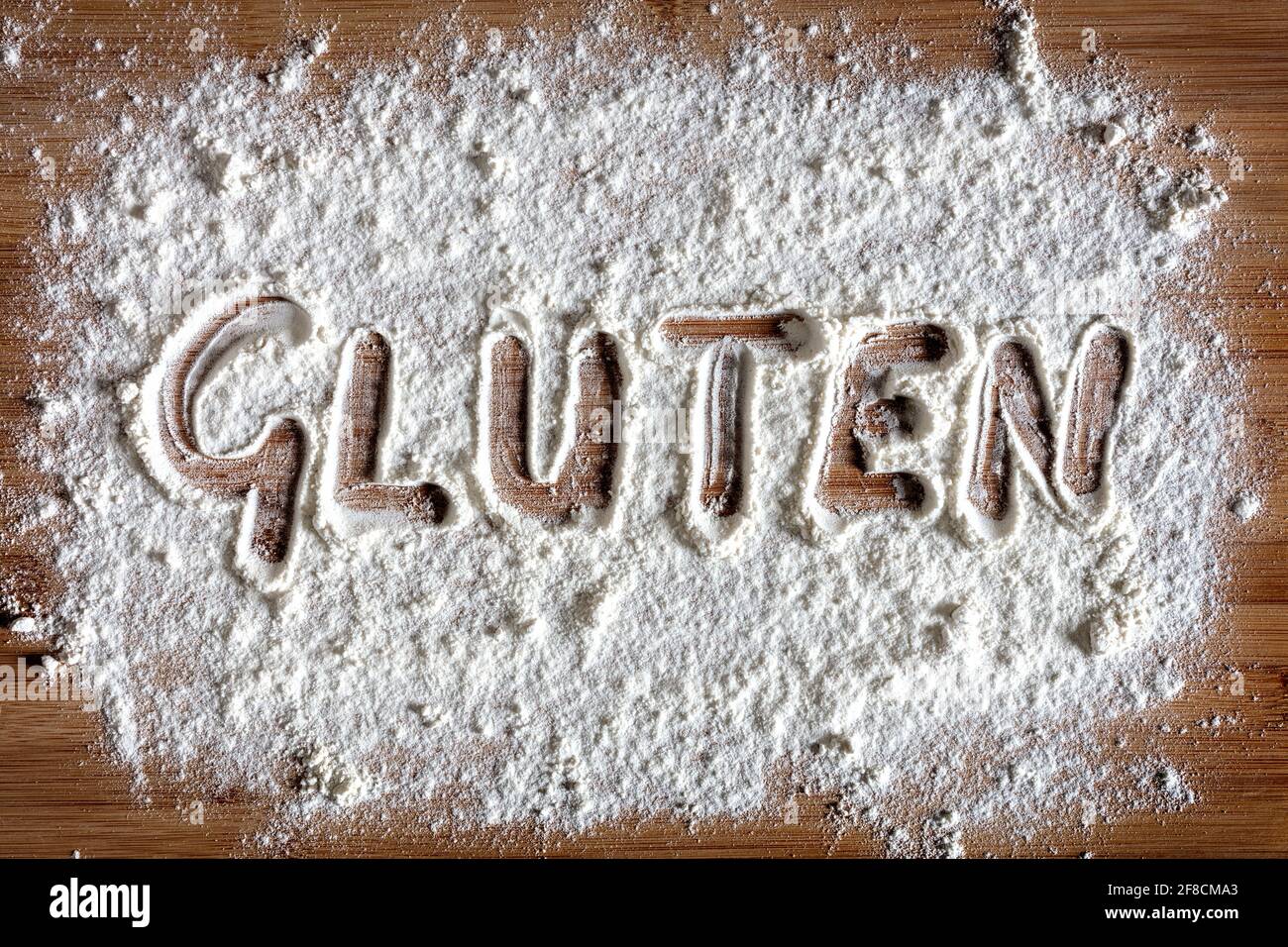 Parola di glutine scritta nel concetto di farina su tavola da forno per cura degli allergeni e intolleranza Foto Stock