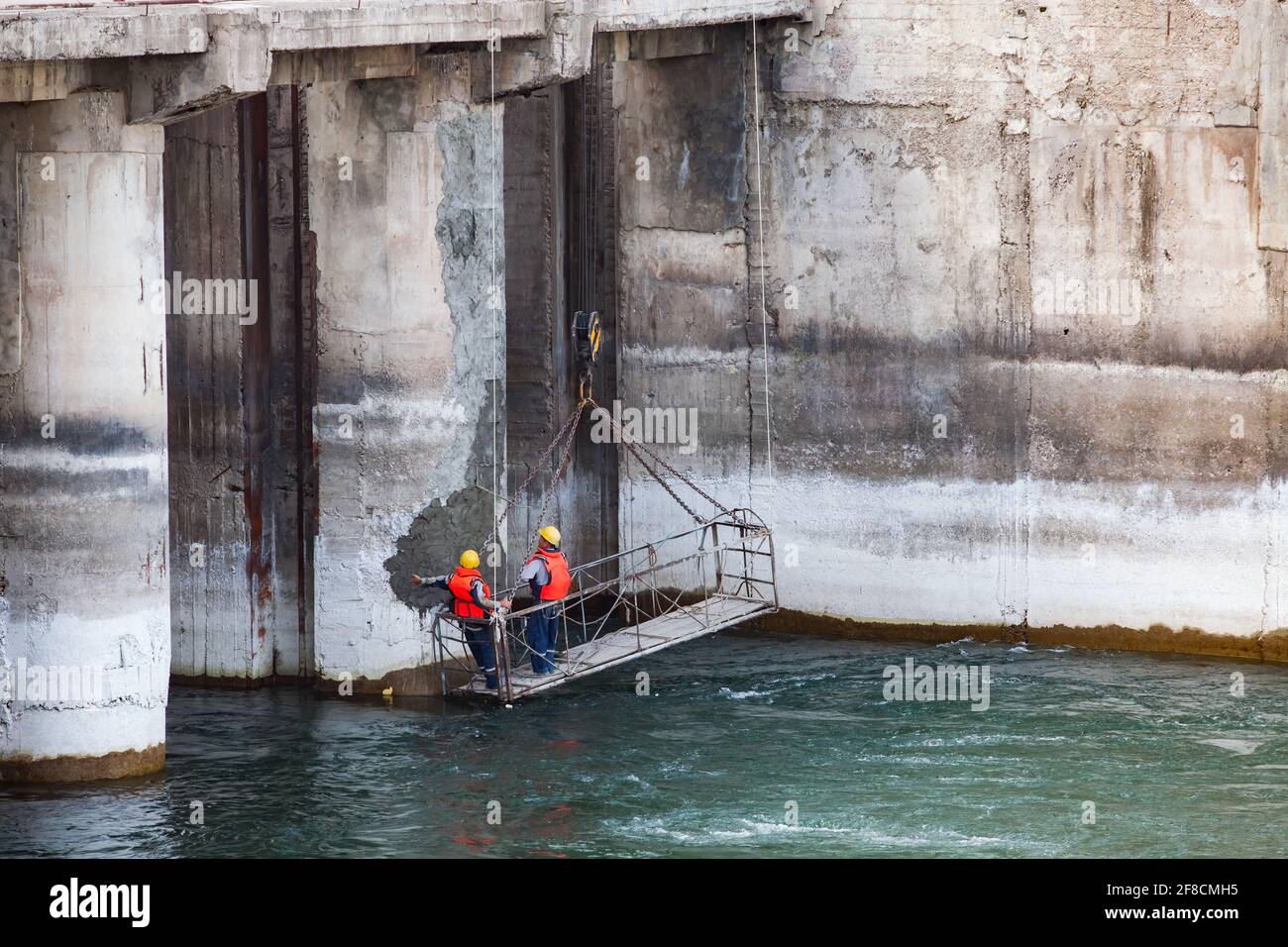 Due tecnici addetti alla manutenzione o tecnici in culla sospesa che guardano la diga del fiume Shardara. Controllo della qualità del calcestruzzo Foto Stock