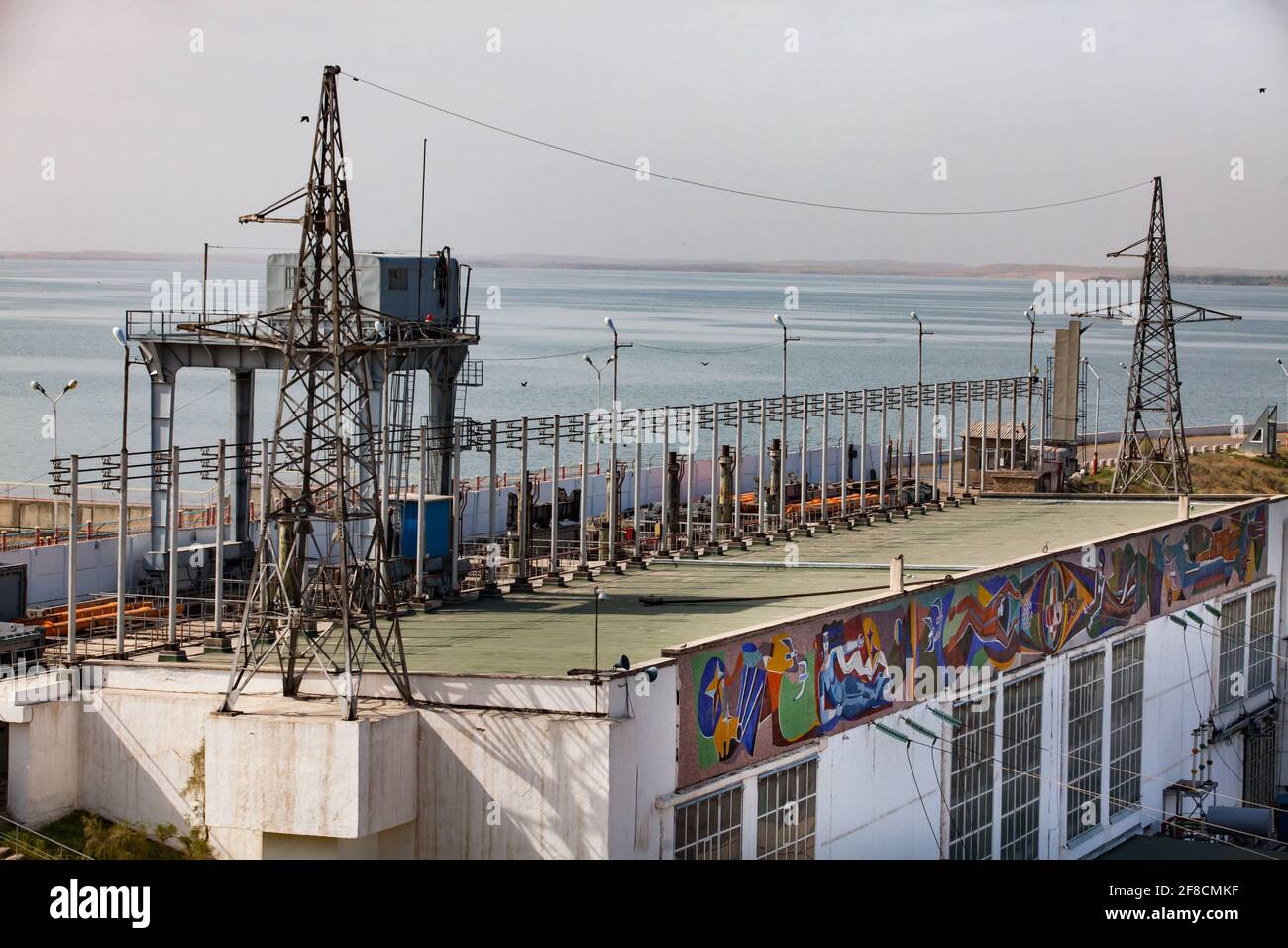 Impianto idroelettrico di Shardara. Diga, edificio principale, autobus elettrici e gru a portale con cabina. Deposito di acqua di Shardara sullo sfondo. Kazakistan. Foto Stock