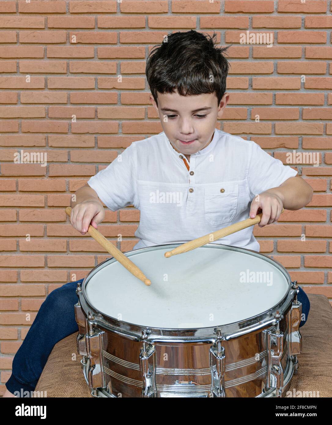 il bambino di 7 anni si concentrò e suonando la batteria. Muro di mattoni  sfondo Foto stock - Alamy