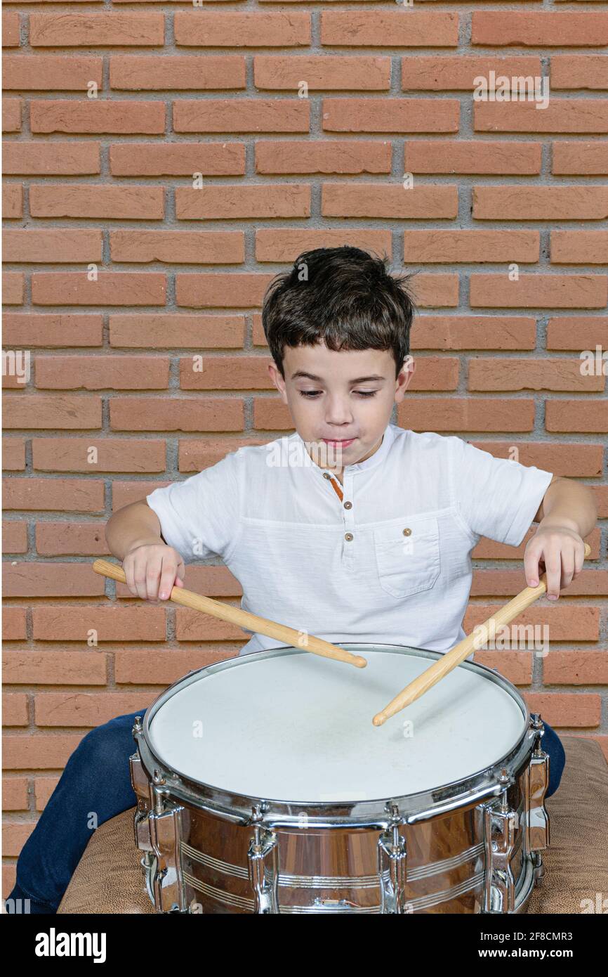 bambino di 7 anni che suona la batteria e fa una faccia divertente. Muro di  mattoni sfondo Foto stock - Alamy
