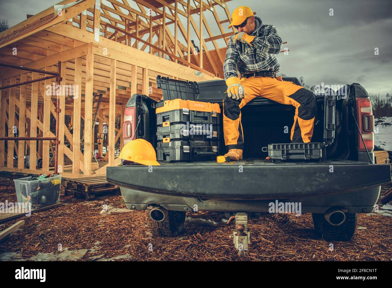 Contraente di costruzione sul suo camion del raccoglitore vicino al telaio dello scheletro della casa di legno. Tema dell'industria delle costruzioni. Foto Stock