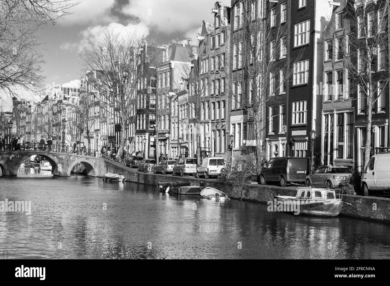 Amsterdam, Paesi Bassi - 24 febbraio 2017: Vista in bianco e nero sul canale di Amsterdam, la gente comune cammina sulla costa vicino a vecchie case viventi Foto Stock