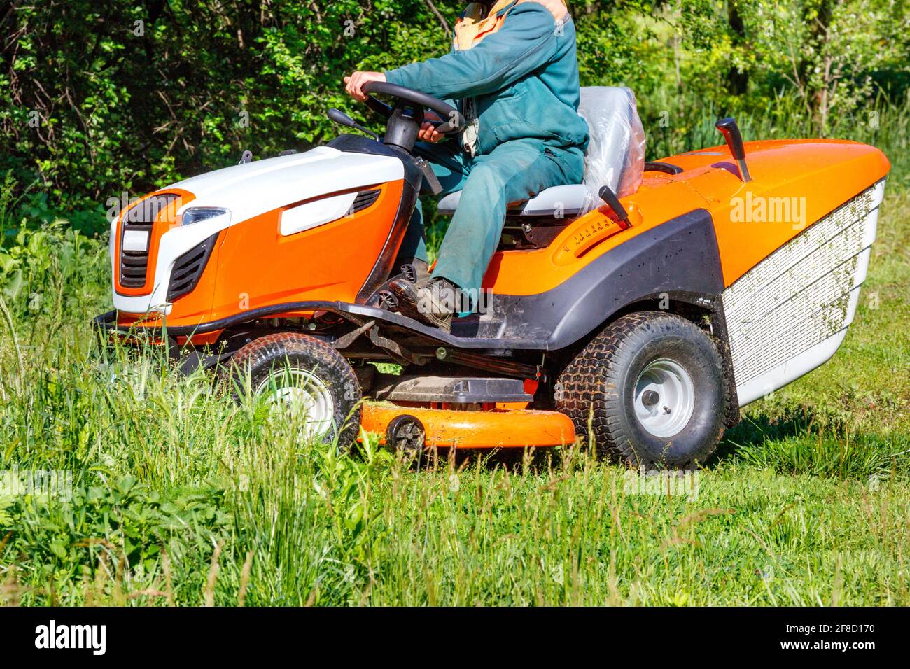 Un giardiniere seduto su un trattore professionale tosaerba raschia erba  verde alta in un prato troppo cresciuto in una chiara giornata di sole.  Spazio di copia Foto stock - Alamy