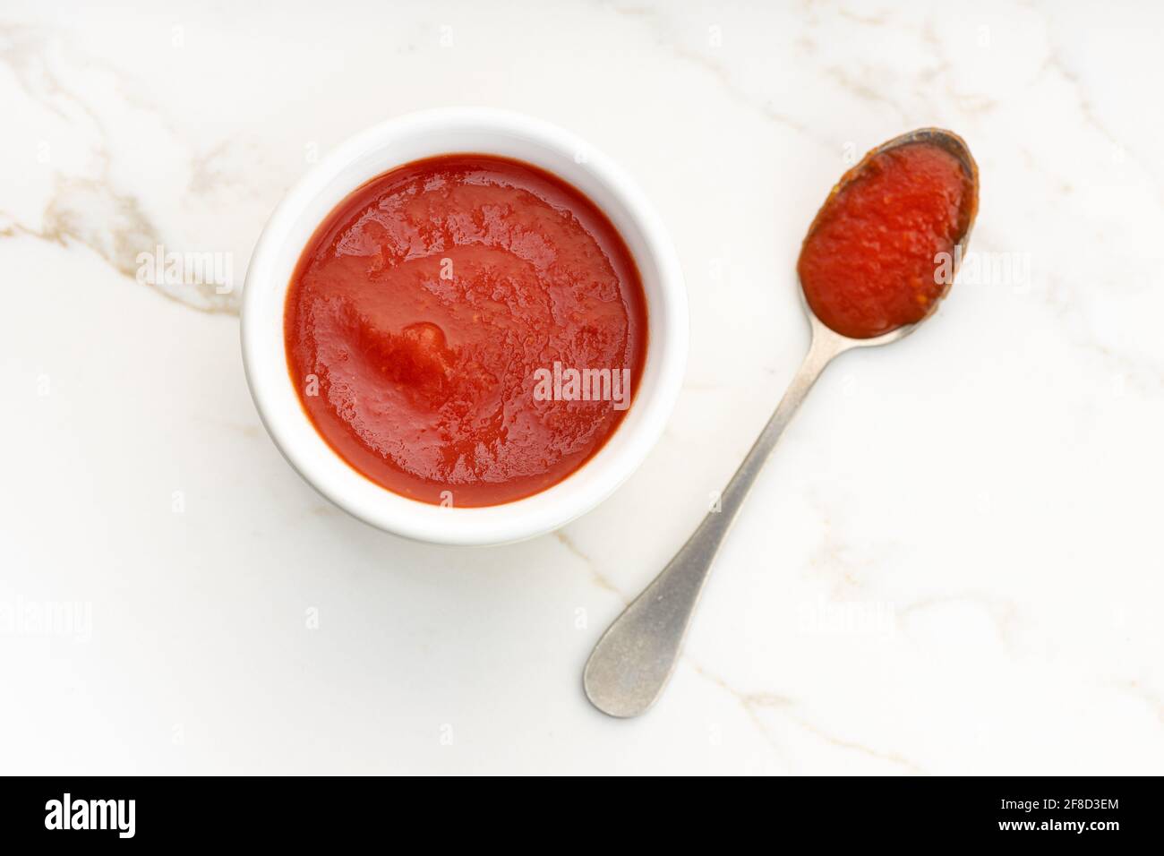 Salsa di pomodoro fresca su recipiente e cucchiaio su tavolo di marmo bianco. Vista dall'alto Foto Stock