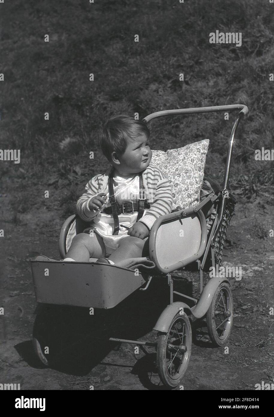 Anni '50, storico, fuori in un giorno d'estate, un bambino bambino, seduto in un passeggino con struttura in metallo o buggy dell'epoca, con poggiapiedi attaccato e un cuscino per sostegno alla schiena, Inghilterra, Regno Unito. Foto Stock