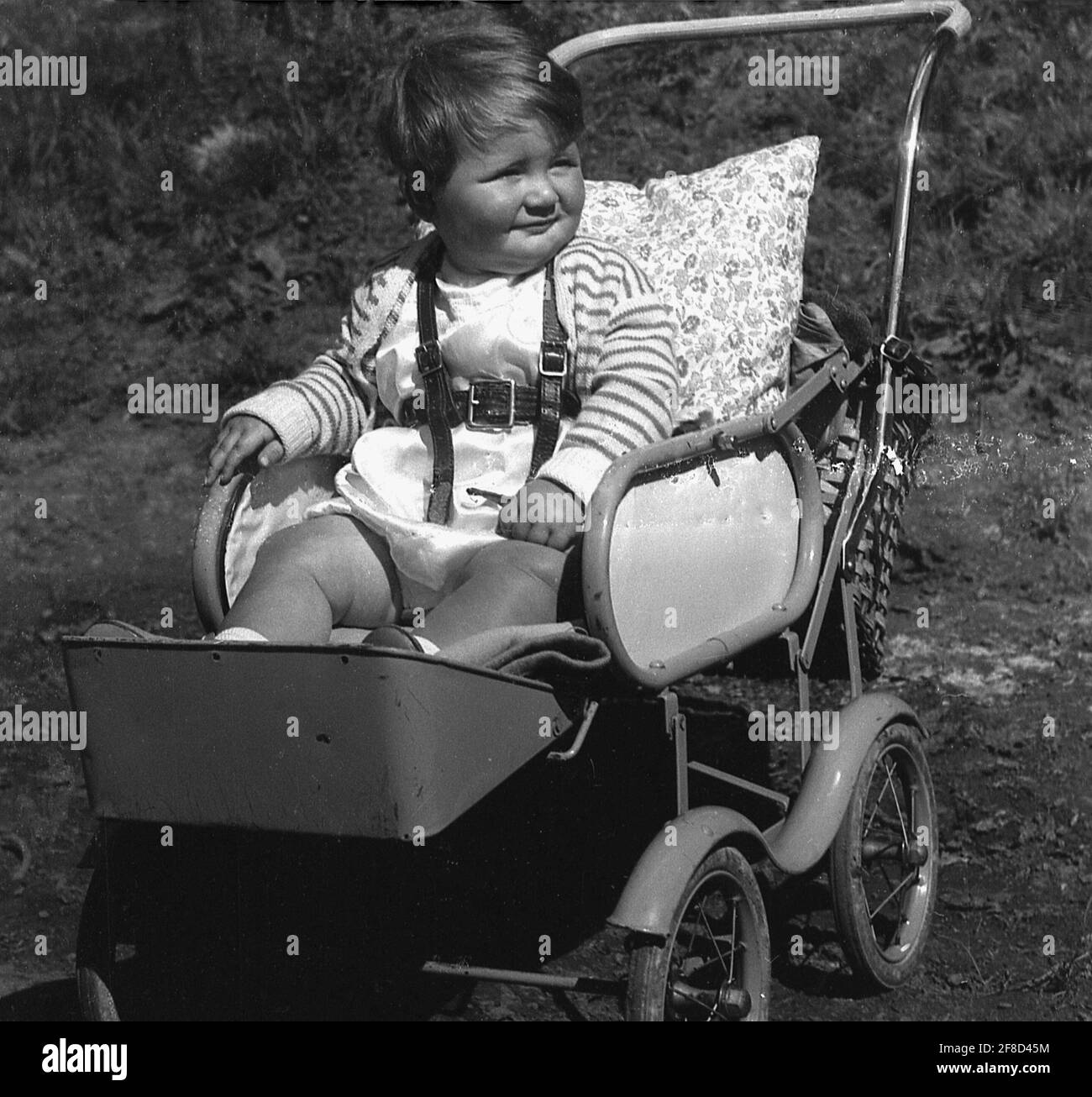 Anni '50, storico, fuori in un giorno d'estate, un bambino bambino seduto in una struttura in metallo pushchair o buggy dell'epoca, con poggiapiedi attaccato e un cuscino per sostegno schiena, Inghilterra, Regno Unito. Foto Stock