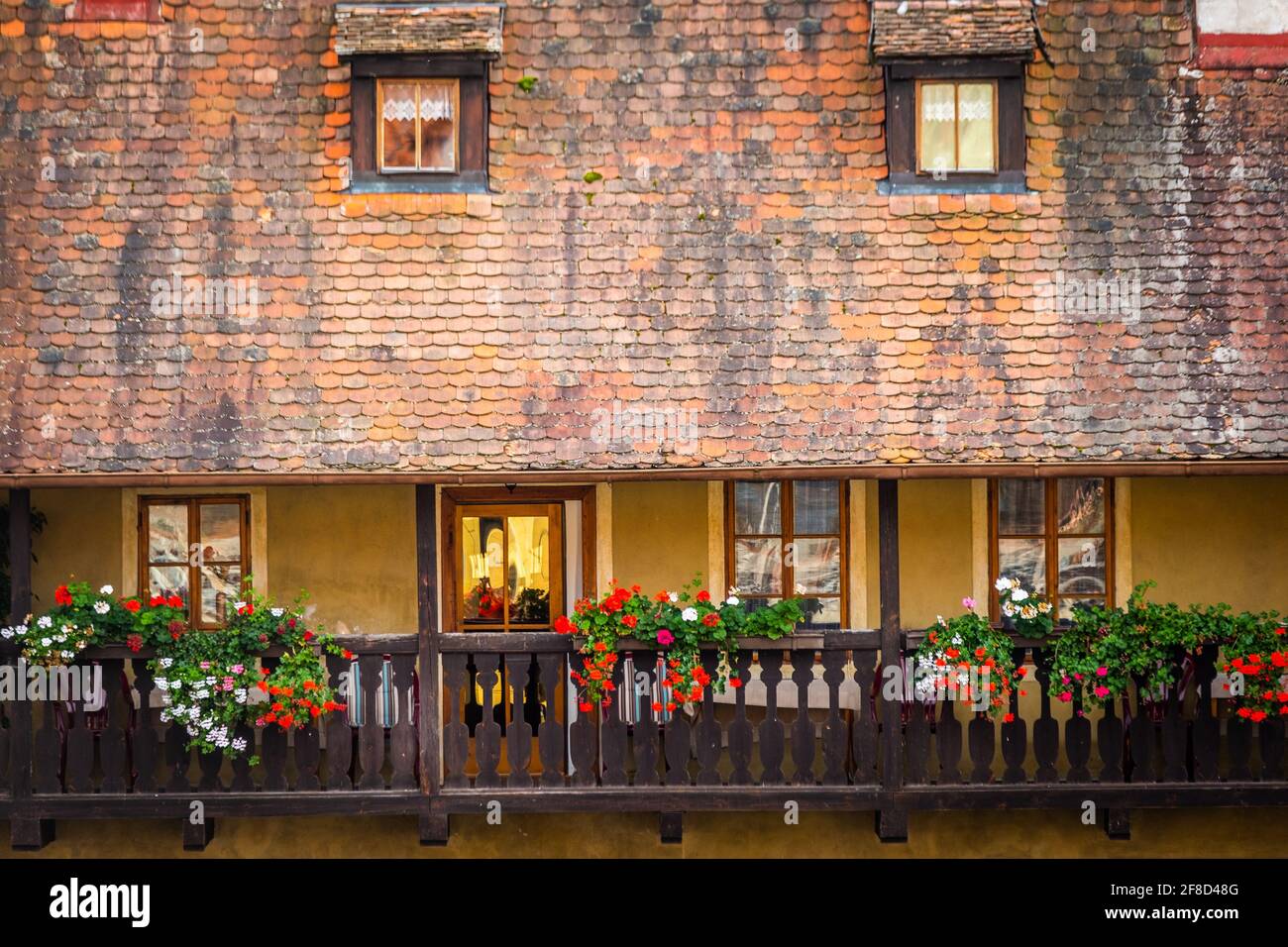 Vista del vecchio edificio giallo con tegole arancioni e. balcone in legno con vasi da fiori Foto Stock