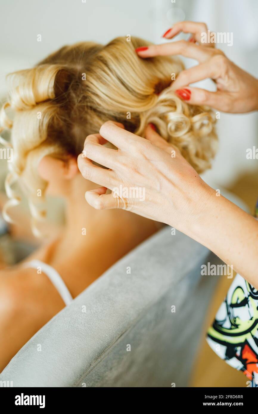 Stilista facendo capelli alla sposa bionda durante la preparazione per la cerimonia nuziale, primo piano Foto Stock