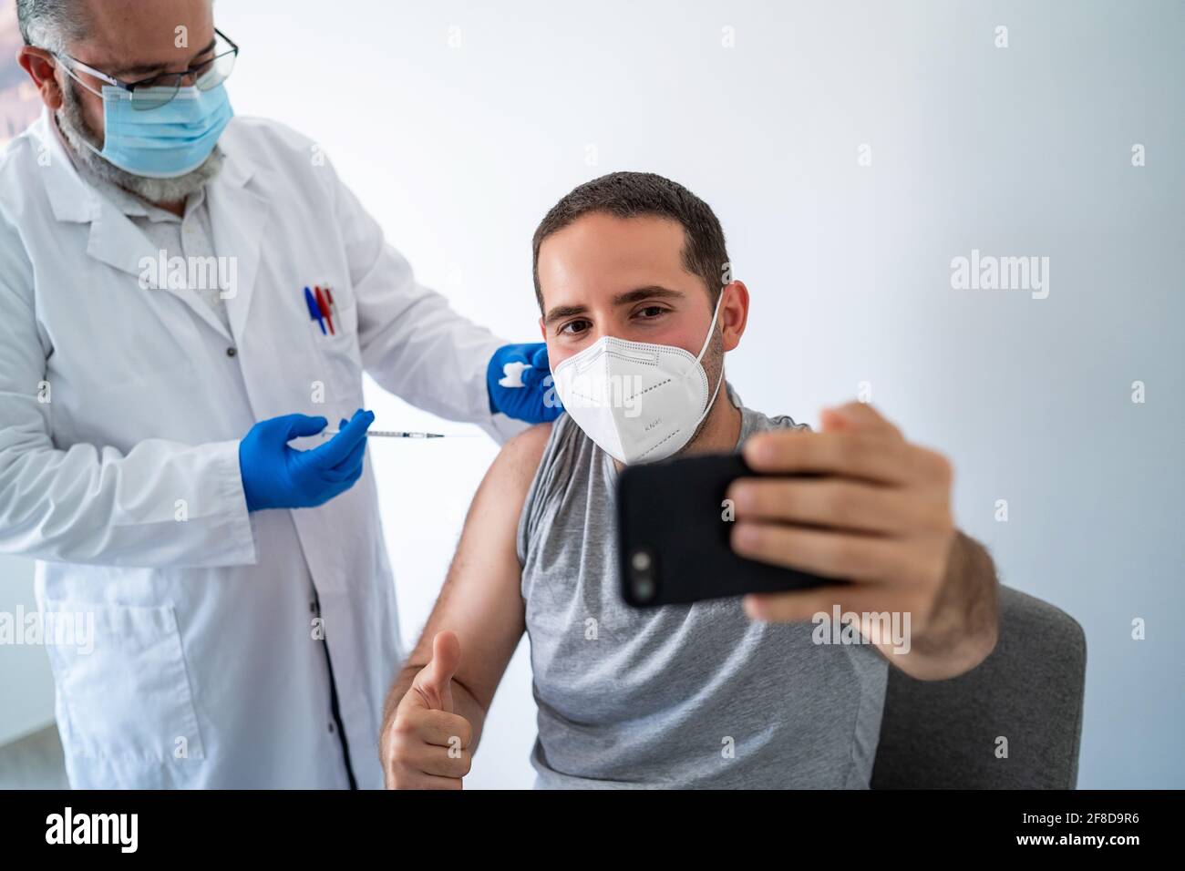 Medico vaccinare un giovane uomo mentre prende un selfie Foto Stock