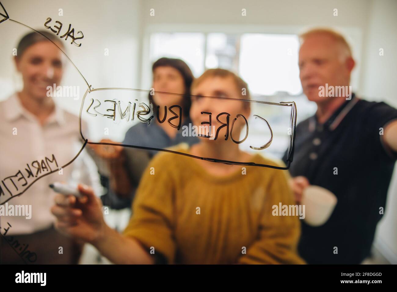 donna d'affari che collabora con colleghi che pianificano un progetto di avvio, scrivendo su una parete di vetro. uomini d'affari che discutono idee durante le riunioni. Foto Stock