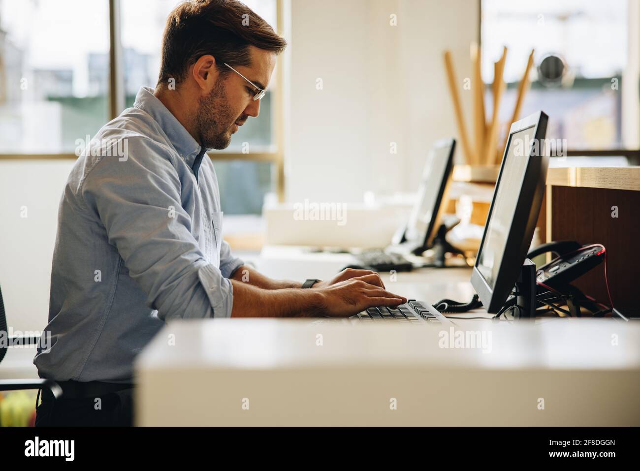 Freelance che scrive sulla tastiera del computer in ufficio. Giovane uomo seduto alla scrivania che lavora con il computer. Foto Stock