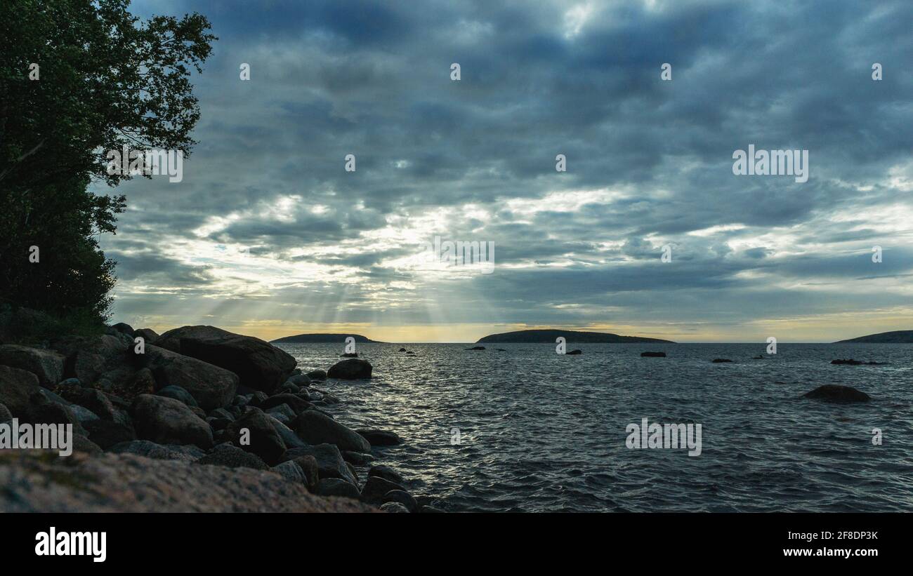 Paesaggio serale sul Mar Bianco. Litorale con massi di pietra. I raggi del sole che si infrangono attraverso le nuvole. Cielo nuvoloso sulla superficie del mare. Il im Foto Stock