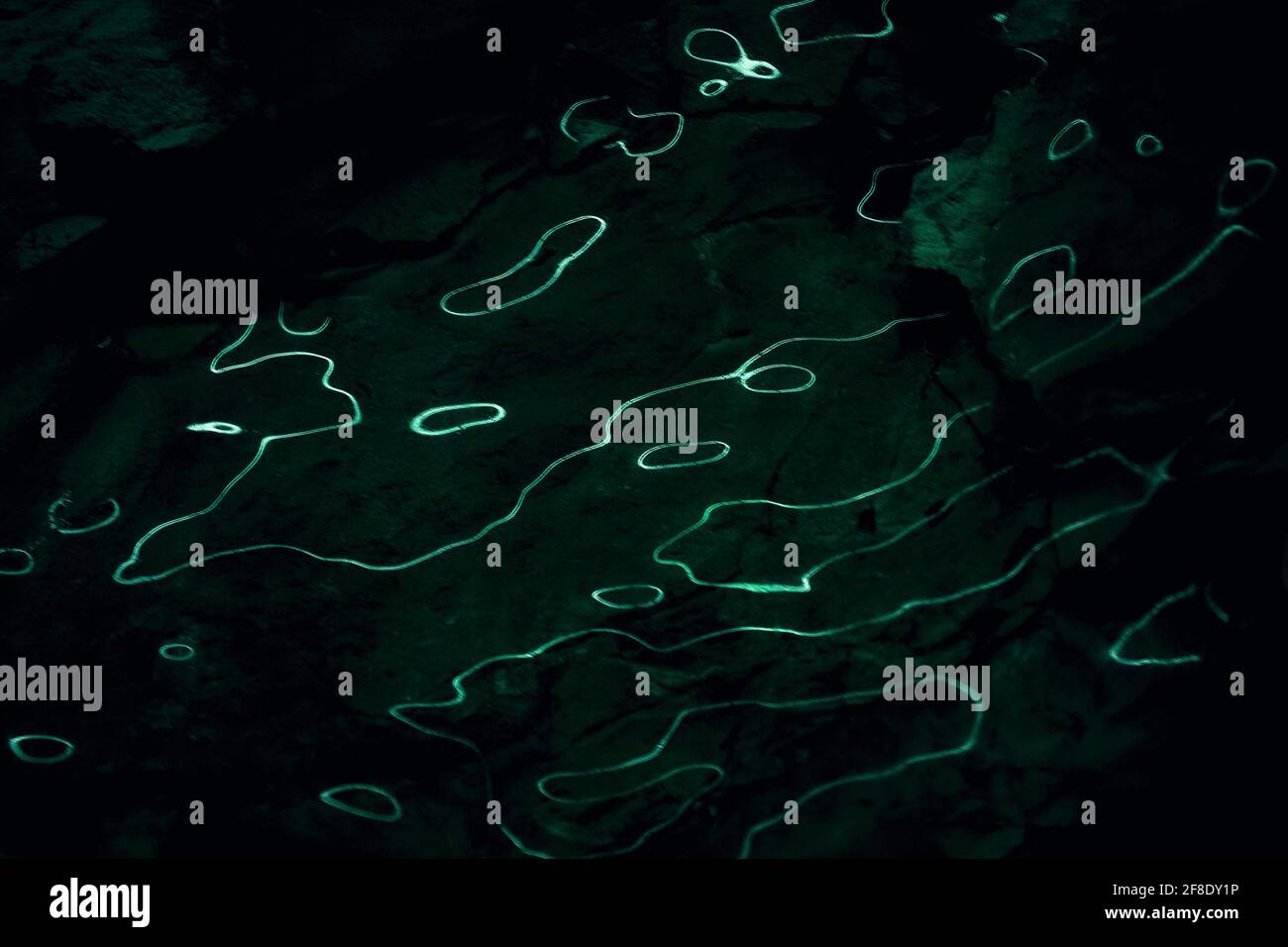 Onde di riflessi chiari su sfondo scuro. Curve astratte della luce fluorescente sulla superficie del ghiaccio. Fondo d'acqua scuro con luci organiche e liquide. Foto Stock