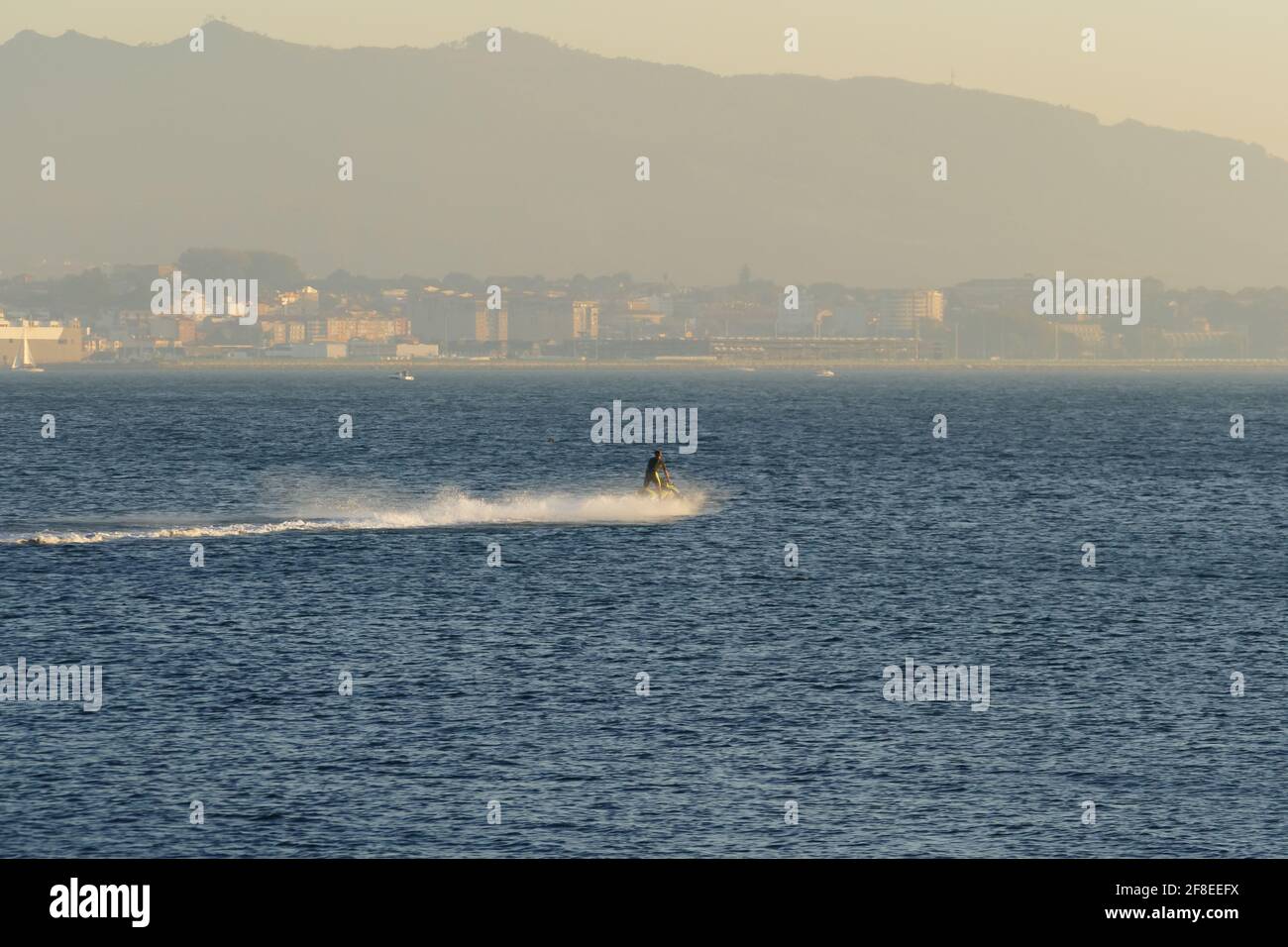 Una persona irriconoscibile guida un jet ski attraverso il mare con Nebbia nella città di Vigo sullo sfondo Spagna in estate Foto Stock