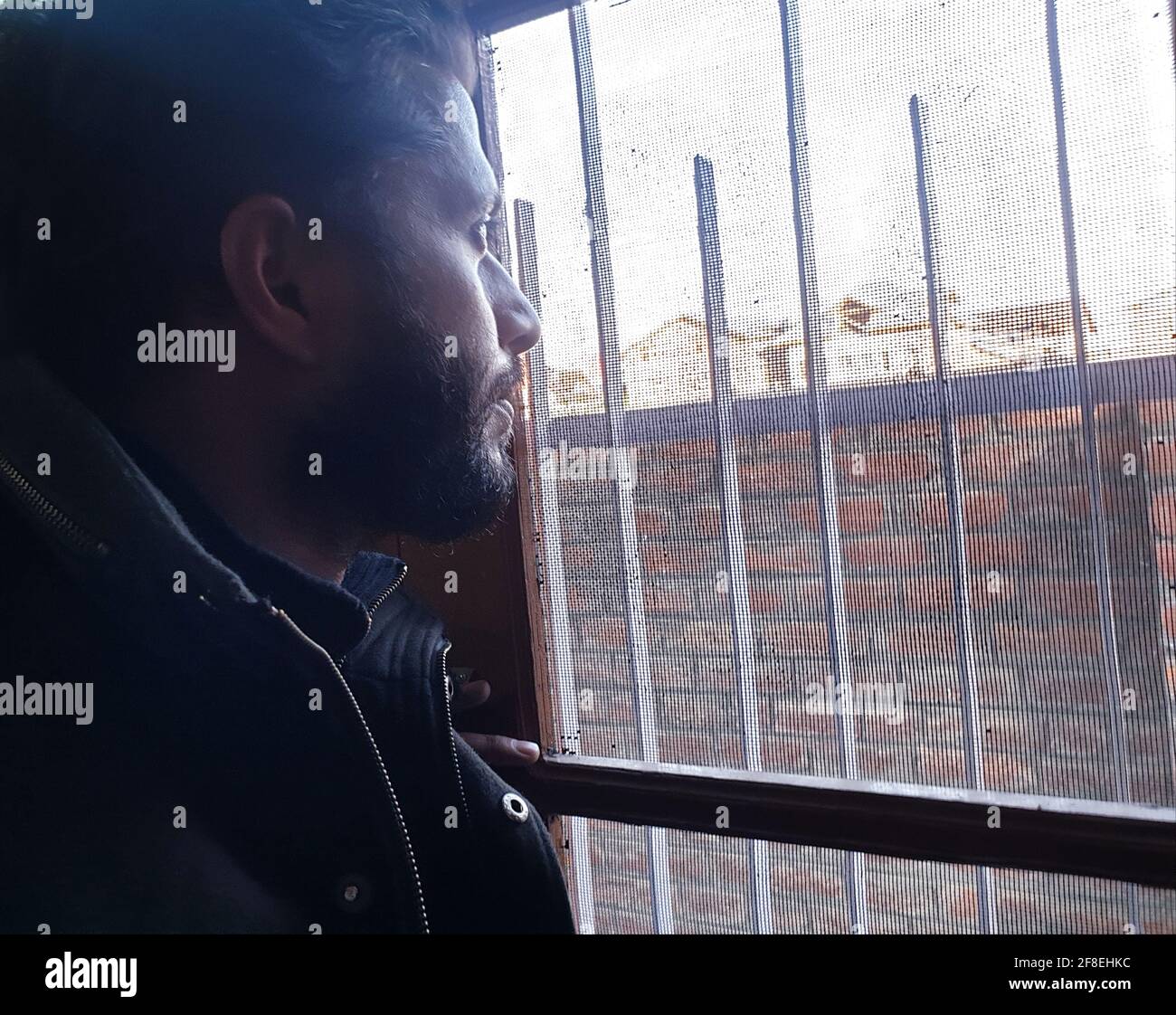 Una persona con maschera protettiva che guarda dalle finestre domestiche. La gente auto-isolando a casa, ha preso attraverso il loro specchio di finestre. Foto Stock