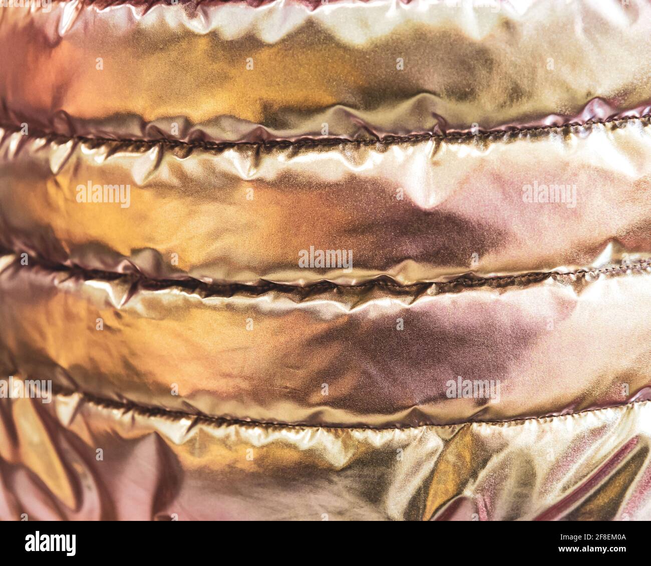La texture dorata iridescente del tessuto bolognese della giacca giovanile trapuntata. Neon rosa in stile trendy sfondo. Foto Stock
