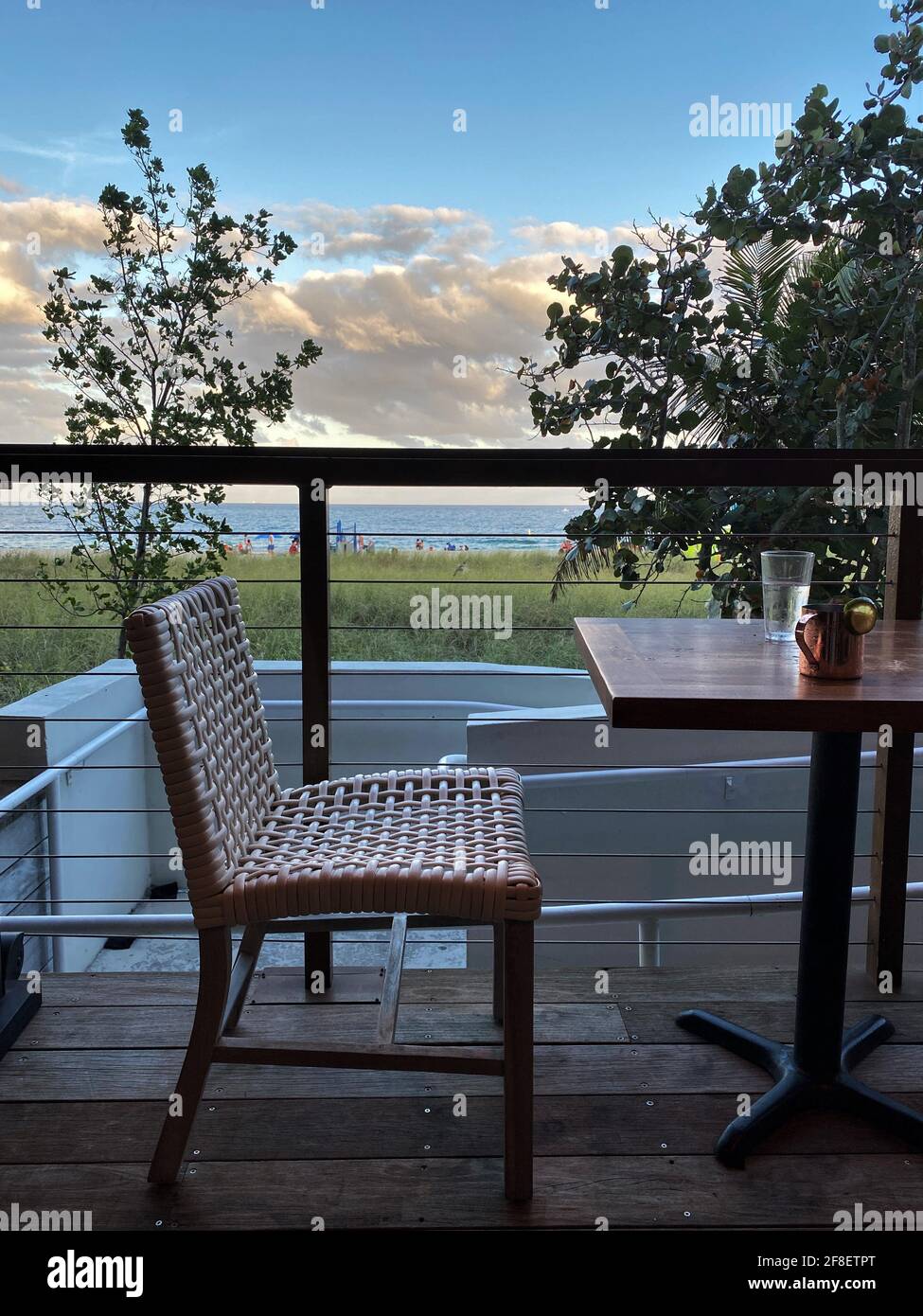 Un drink su un tavolo con una sedia vuota vicino all'oceano durante il tramonto. Concetto di tempo solo, tempo me. Amore di sé, cura di sé Foto Stock