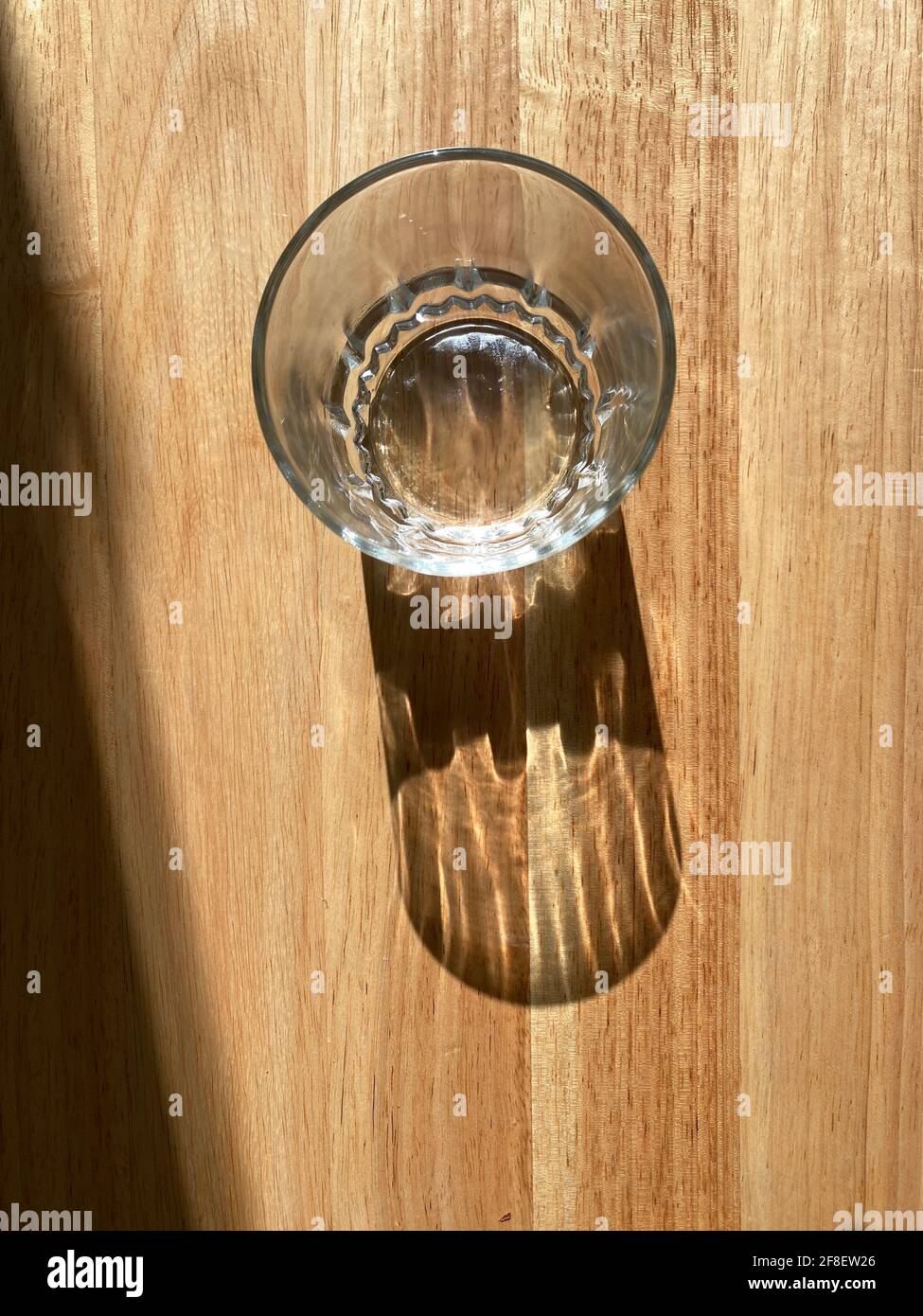 Tazza di vetro vuota su un tavolo di legno con la sua ombra che mostra. Foto Stock