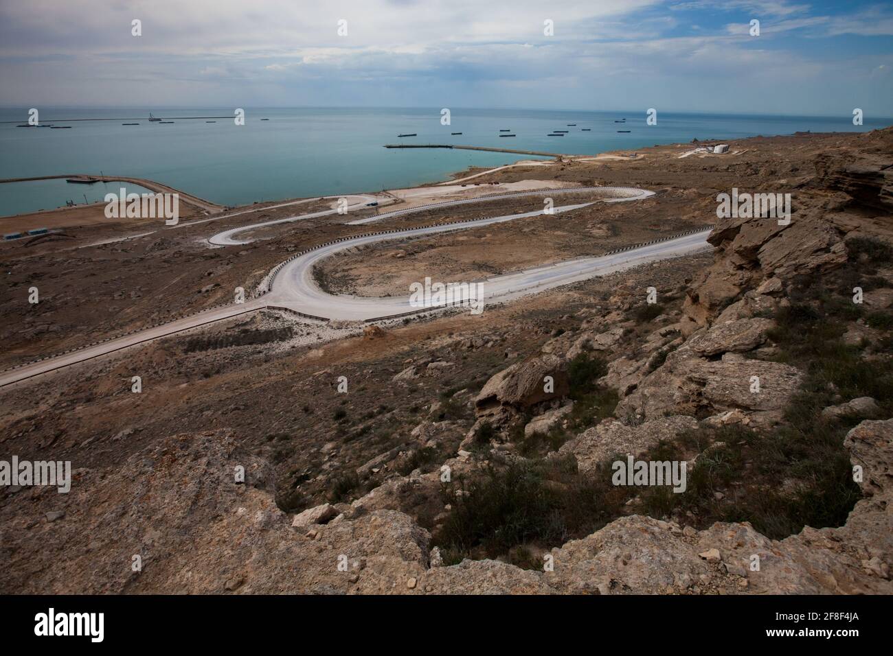 Baia di Bautino, Mangystau, Mar Caspio, Kazakistan. Strada bianca a serpentina fino al mare e al terminal di carico dell'olio. Navi cisterna all'orizzonte. Foto Stock