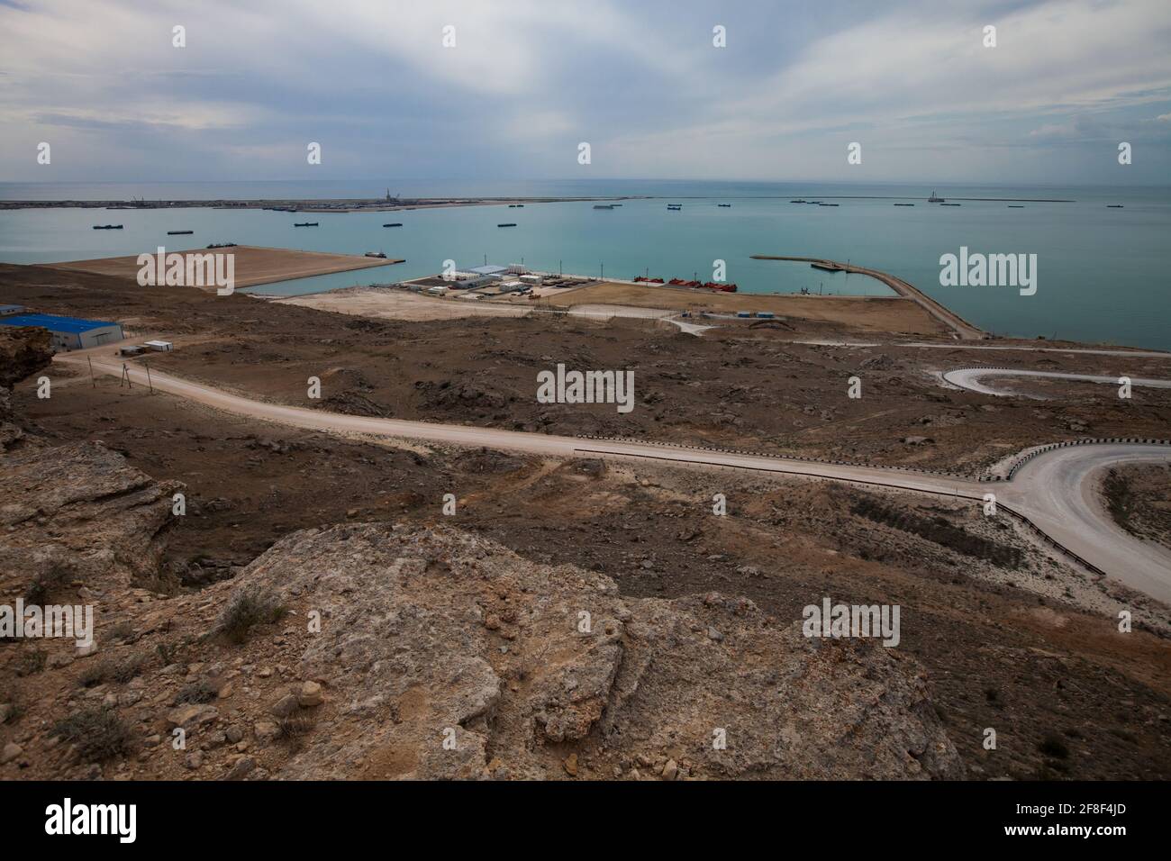 Baia di Bautino, Mangystau, Mar Caspio, Kazakistan. Strada bianca a serpentina fino al mare e al terminal di carico dell'olio. Navi cisterna all'orizzonte. Foto Stock