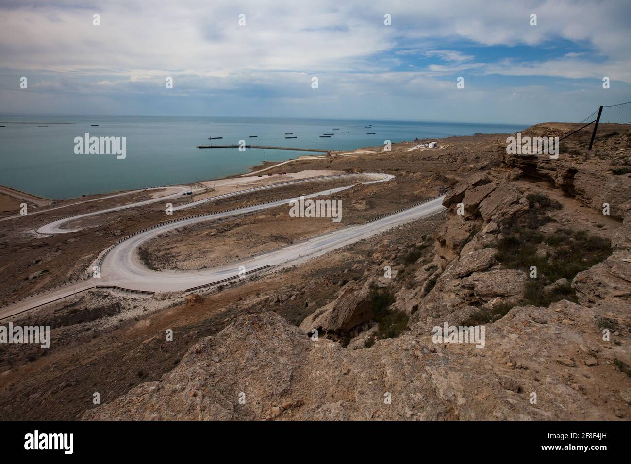 Baia di Bautino, Mangystau, Mar Caspio, Kazakistan. Strada bianca a serpentina fino al mare e al terminal di carico dell'olio. Navi cisterna all'orizzonte. Foto Stock