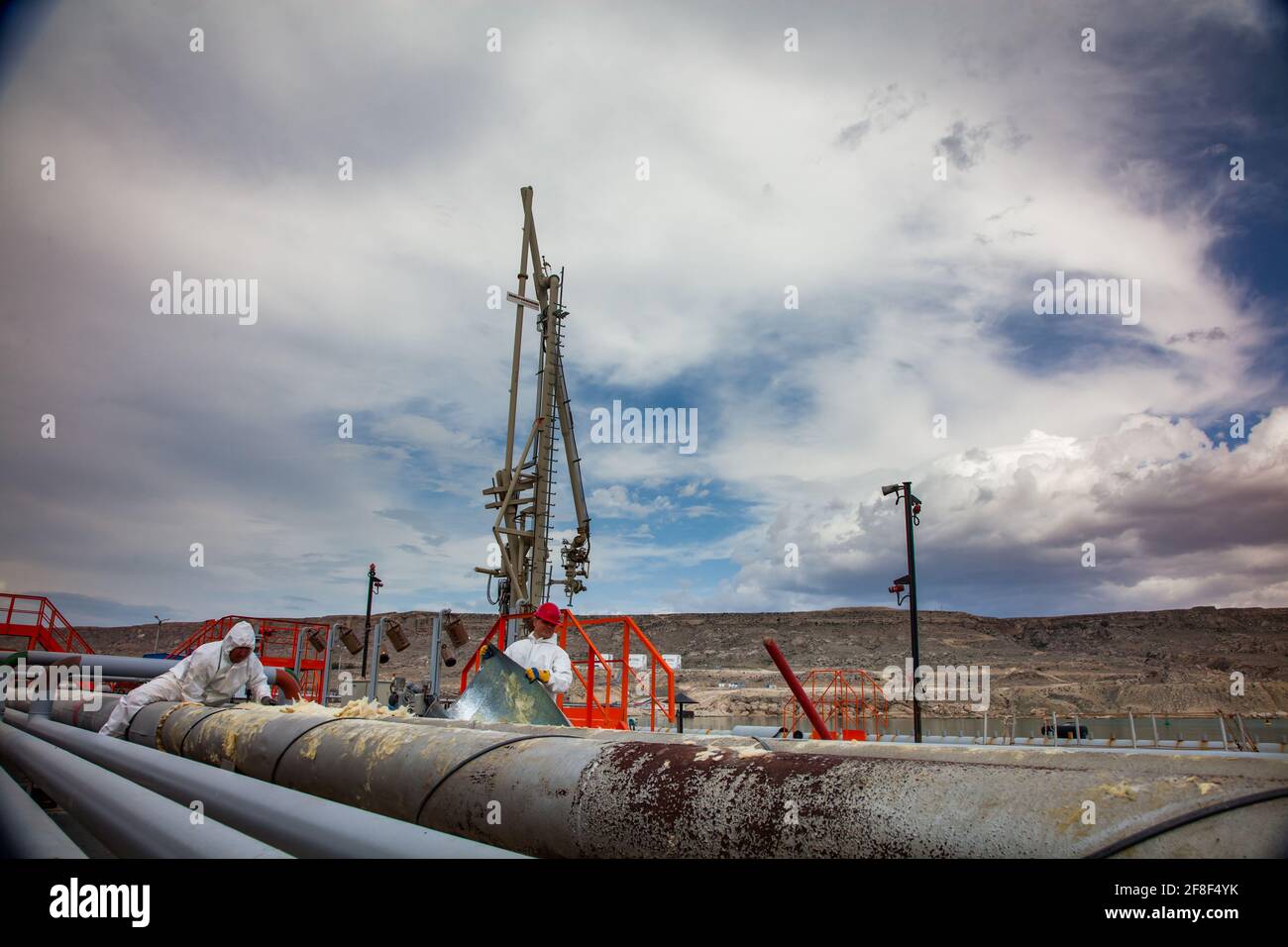 Mangystau, Kazakhstan: Terminal di carico del petrolio sul Mar Caspio. Due operatori in tute di protezione sostituiscono l'isolante termico sui tubi.braccio di carico sullo sfondo. Foto Stock