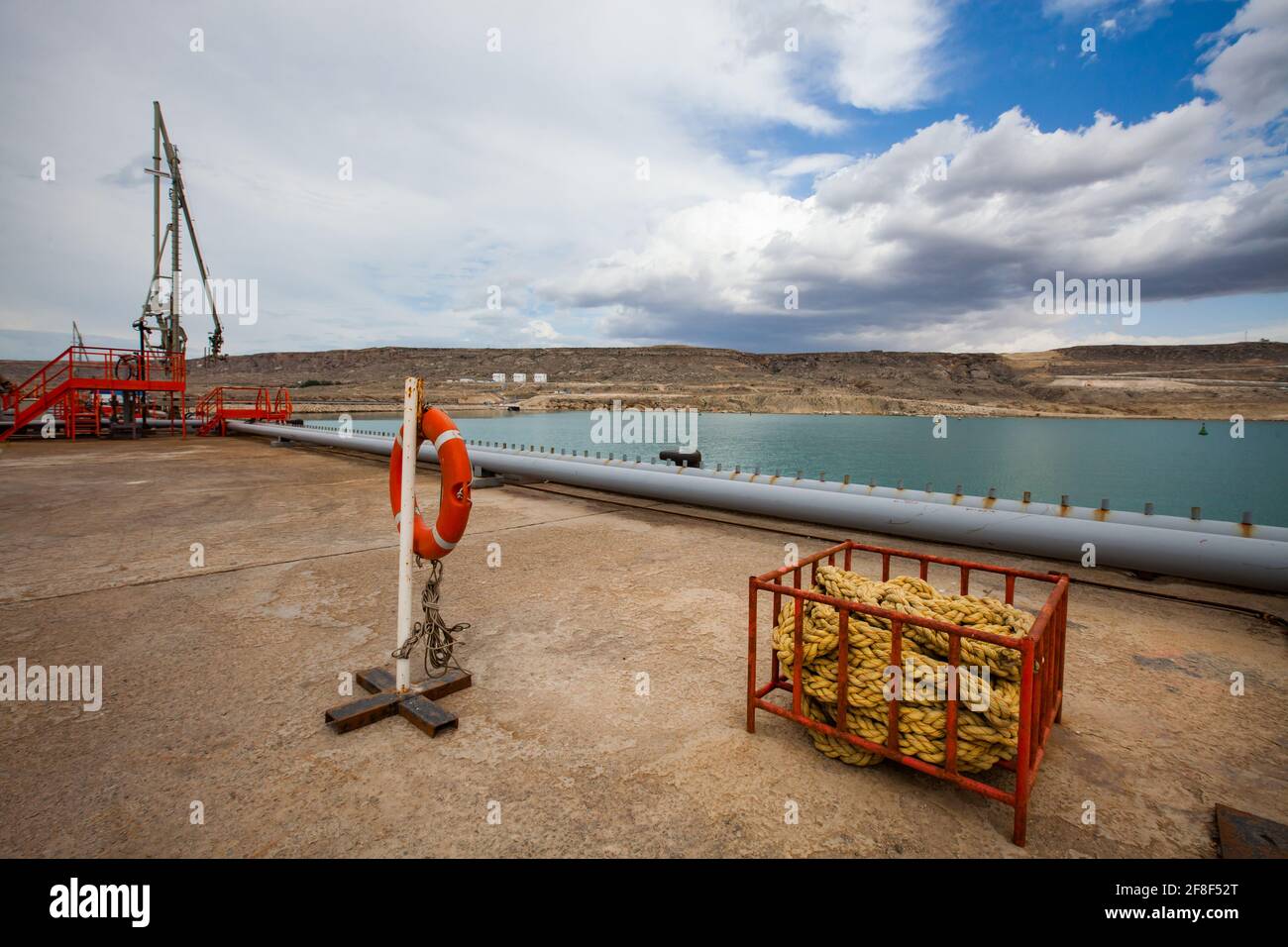 Terminale di riempimento dell'olio per navi cisterna. Articoli di sicurezza. Scale arancioni, balaustra e anello di vita. Pila di corda gialla. Acqua blu e cielo. Foto Stock