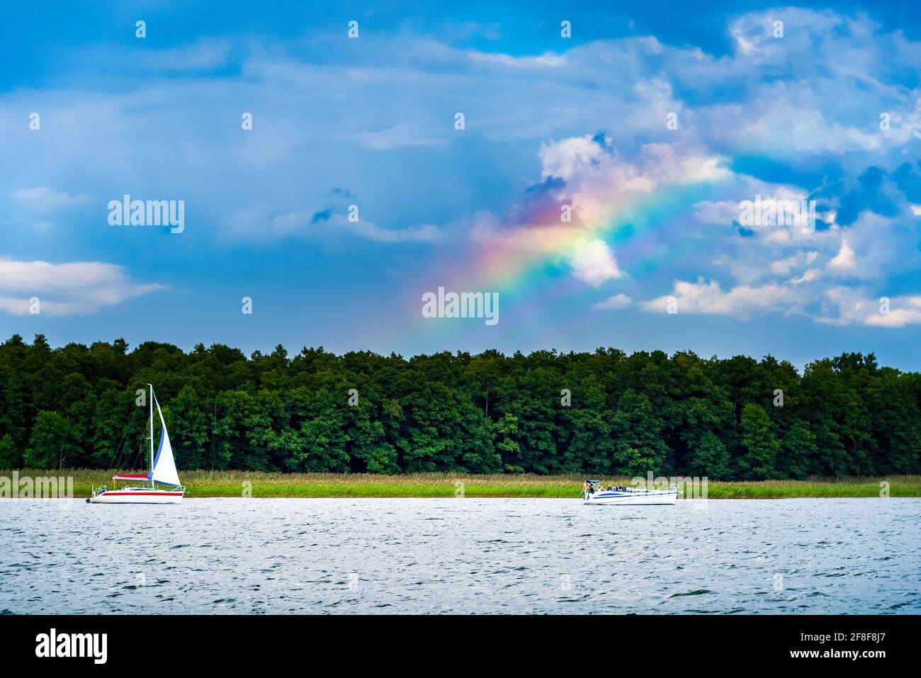 yacht con vela bianca su un lago contro il cupo cielo blu piovoso e l'arcobaleno. vacanza estiva in barca a vela Foto Stock